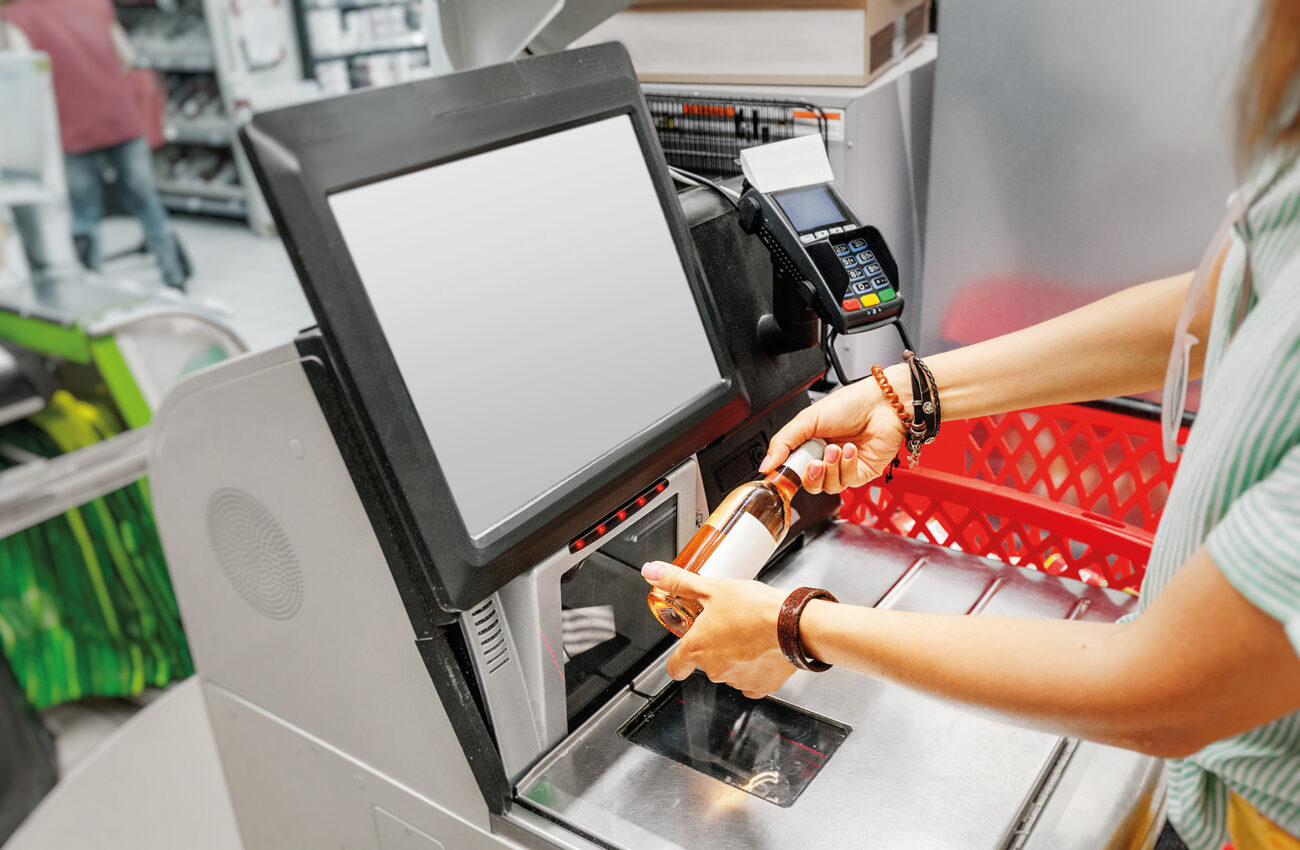 Girl customer scans bottle of wine at the self service checkout in the grocery supermarket shop