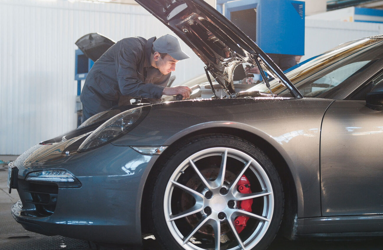 Mechanic male in automobile garage checking hood of the luxury sportcar, telephoto